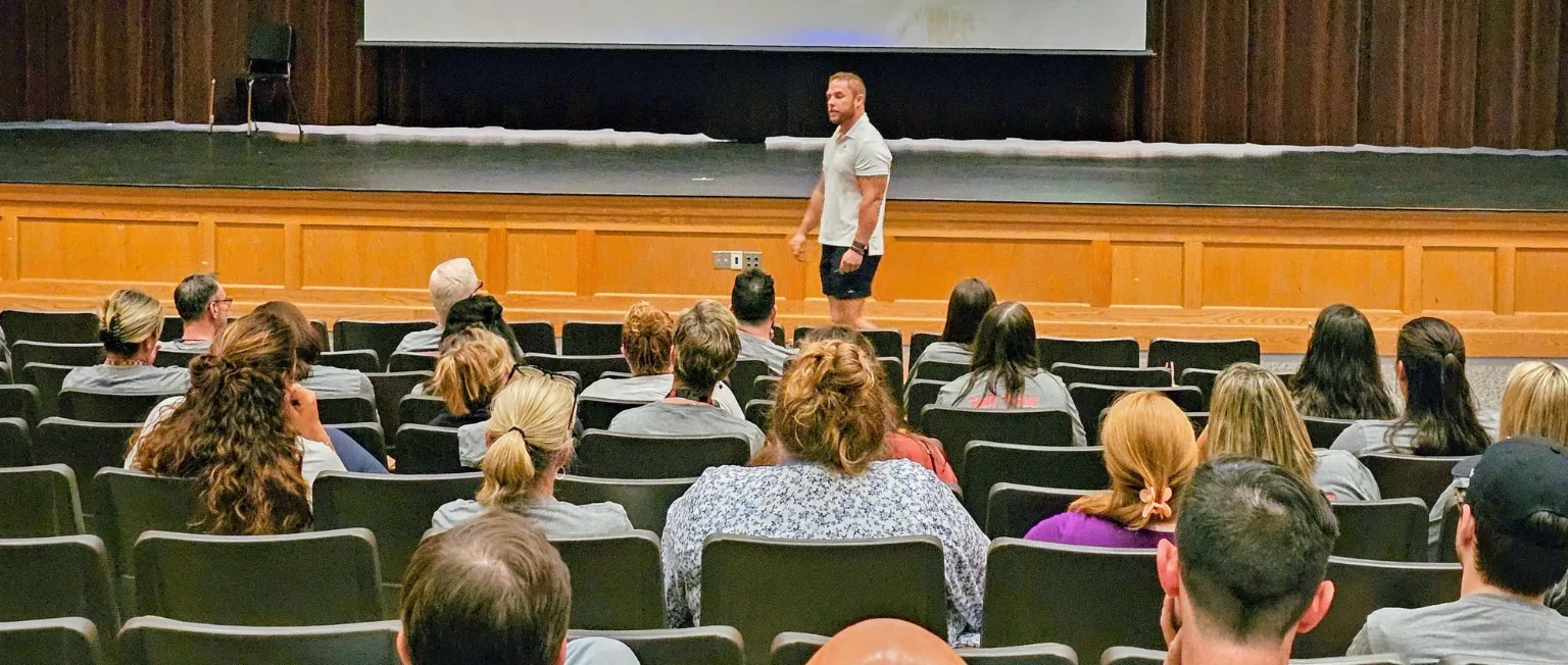 Mike James speaking from the front of an auditorium to a seated audience.